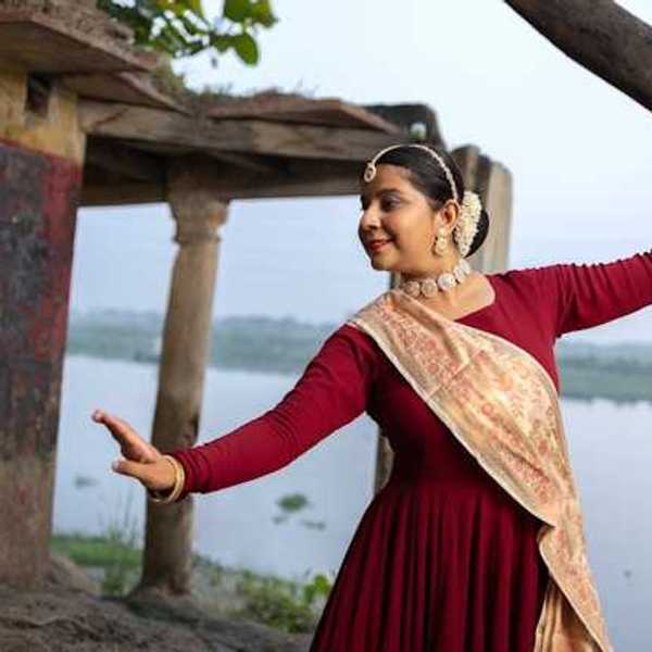 An Indian woman wearing jewerly and a sash dancing next to a river