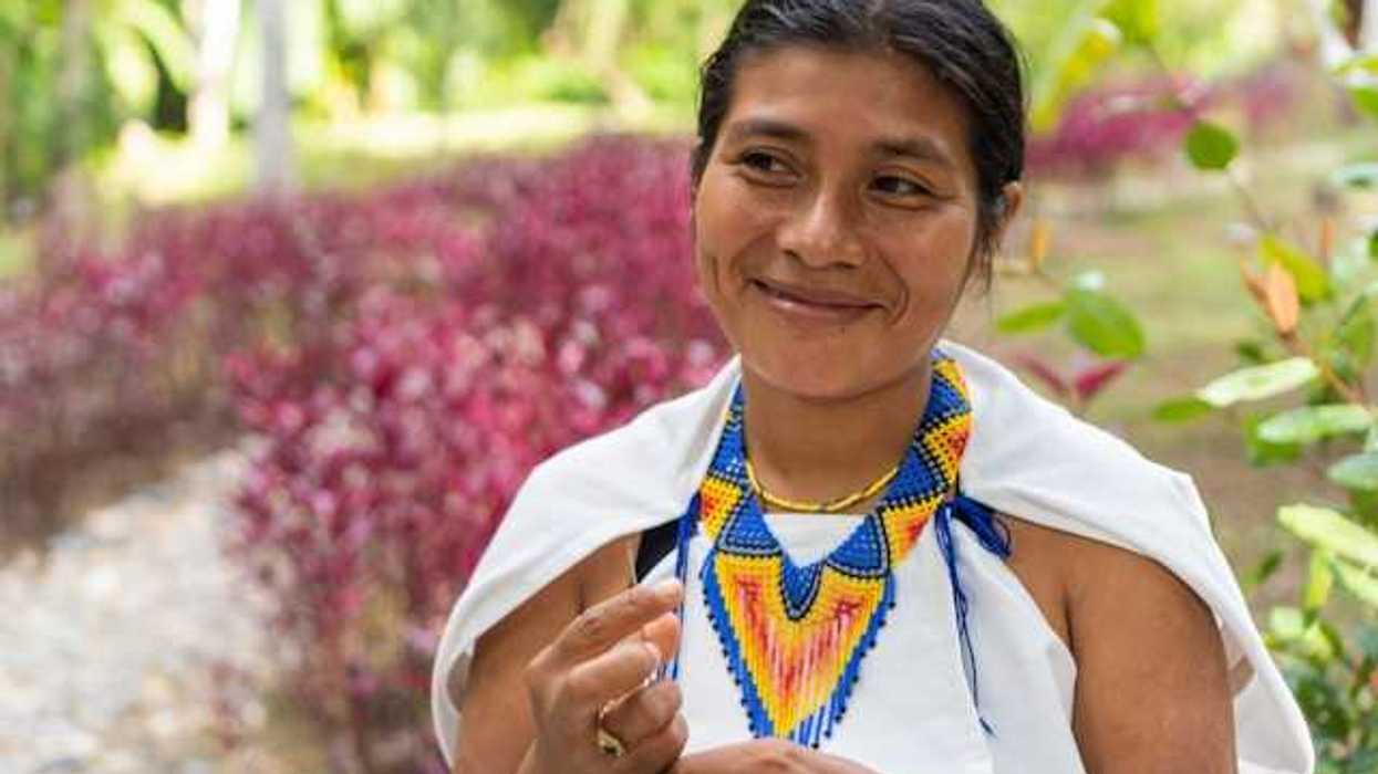 An indigenous woman with a colorful necklace smiling at someone to her right