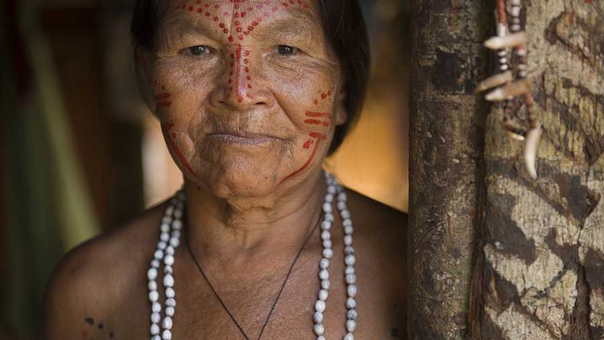 An indigenous woman with red paint on her face standing next to a tree