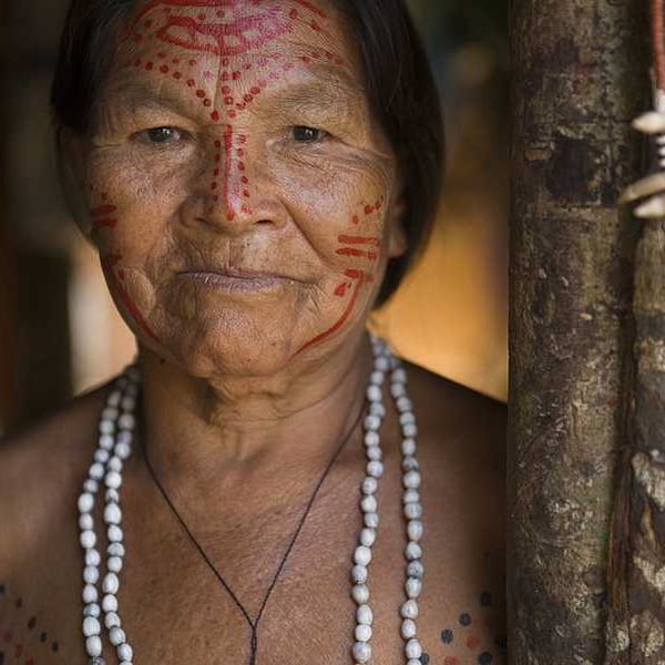 An indigenous woman with red paint on her face standing next to a tree