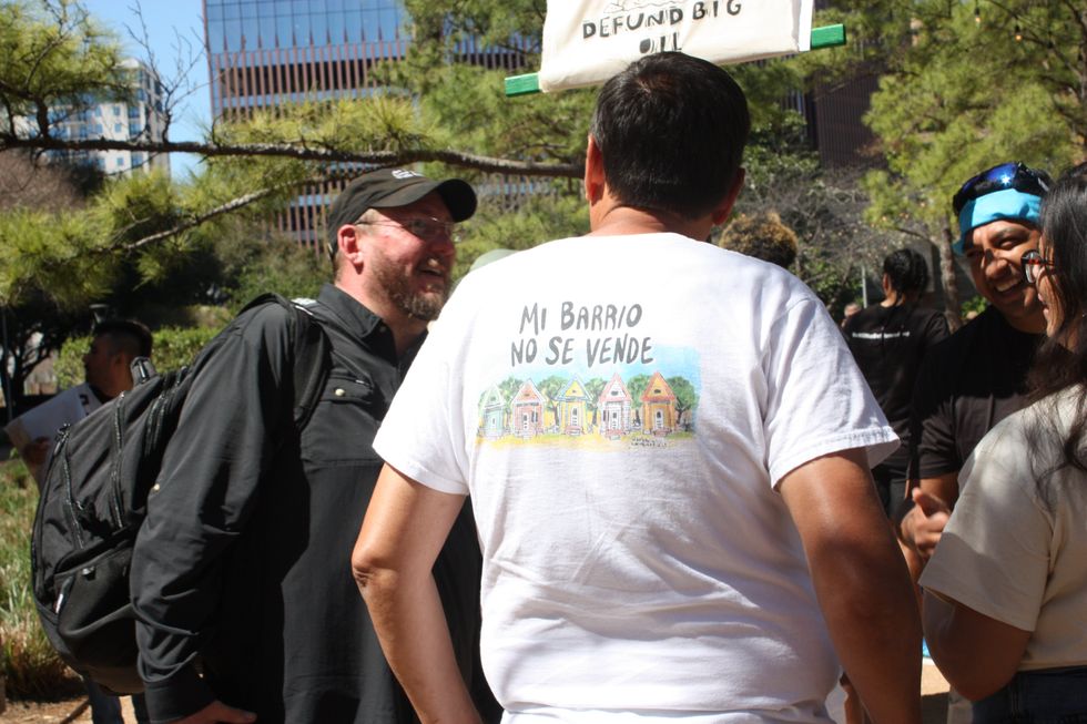 An individual at the protest is wearing a shirt with writing in Spanish that reads, 'My neighborhood isn't for sale.'