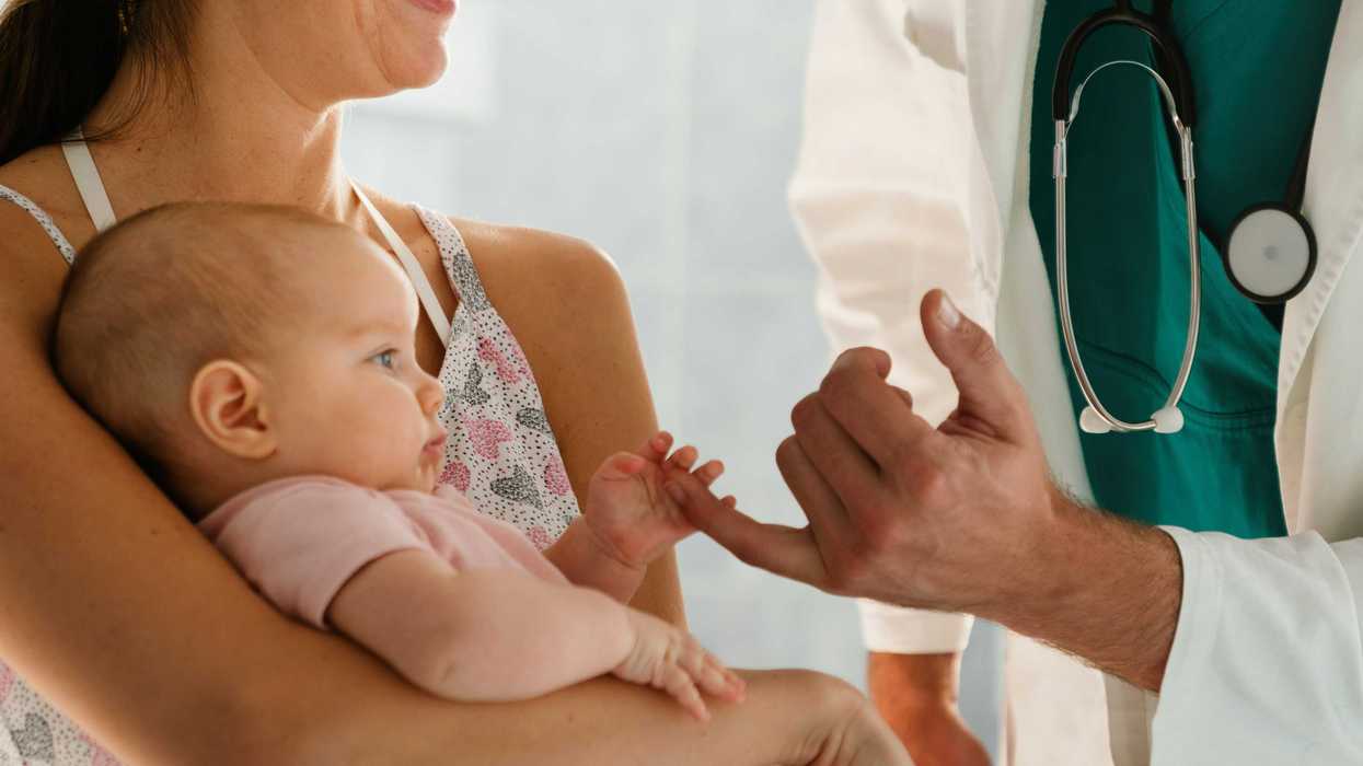 An infant holds a doctor's hand.