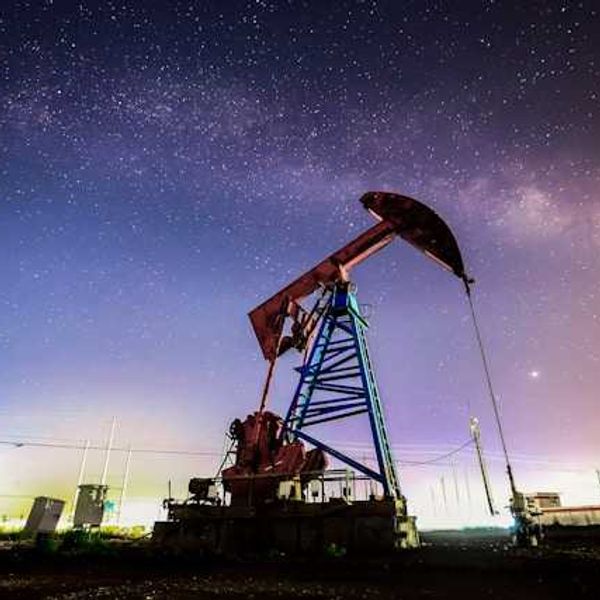 An oil drilling pump jack at night against a starry sky