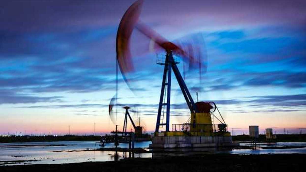 An oil drilling pump jack working in a field a dusk