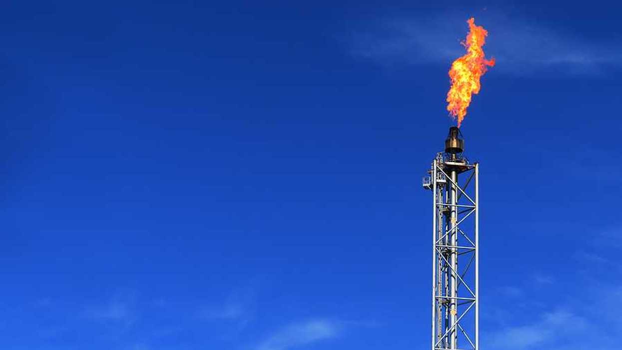 An oil tower with flames during a gas flare against a blue sky