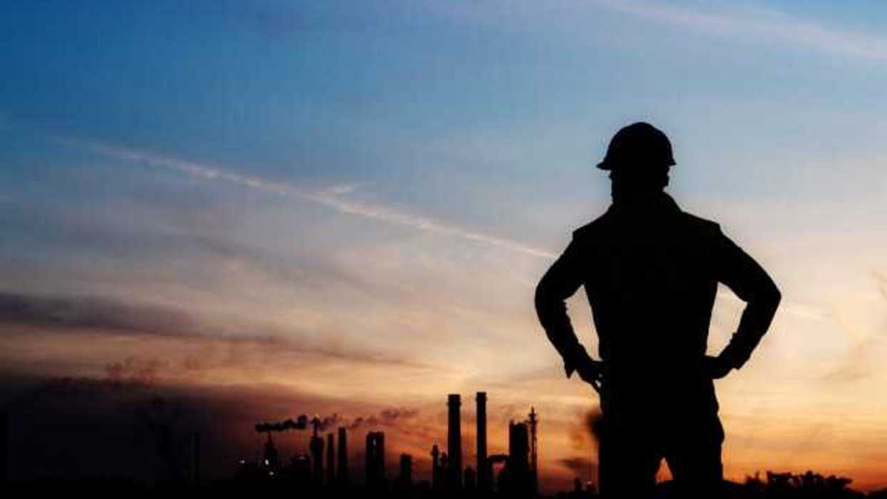 An oil worker silhouetted against a darkening sky and polluting smokestacks in the background