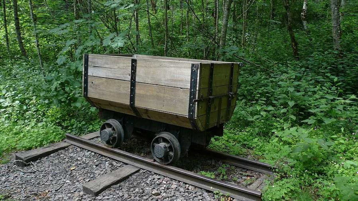 An old wooden mining cart on a rusty set of tracks with a green forest in the background