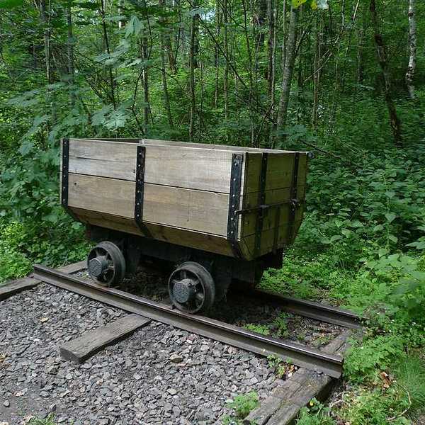 An old wooden mining cart on a rusty set of tracks with a green forest in the background