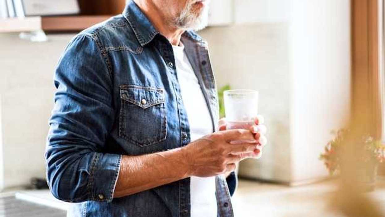 An older gentleman holding a glass of water in the kitchen