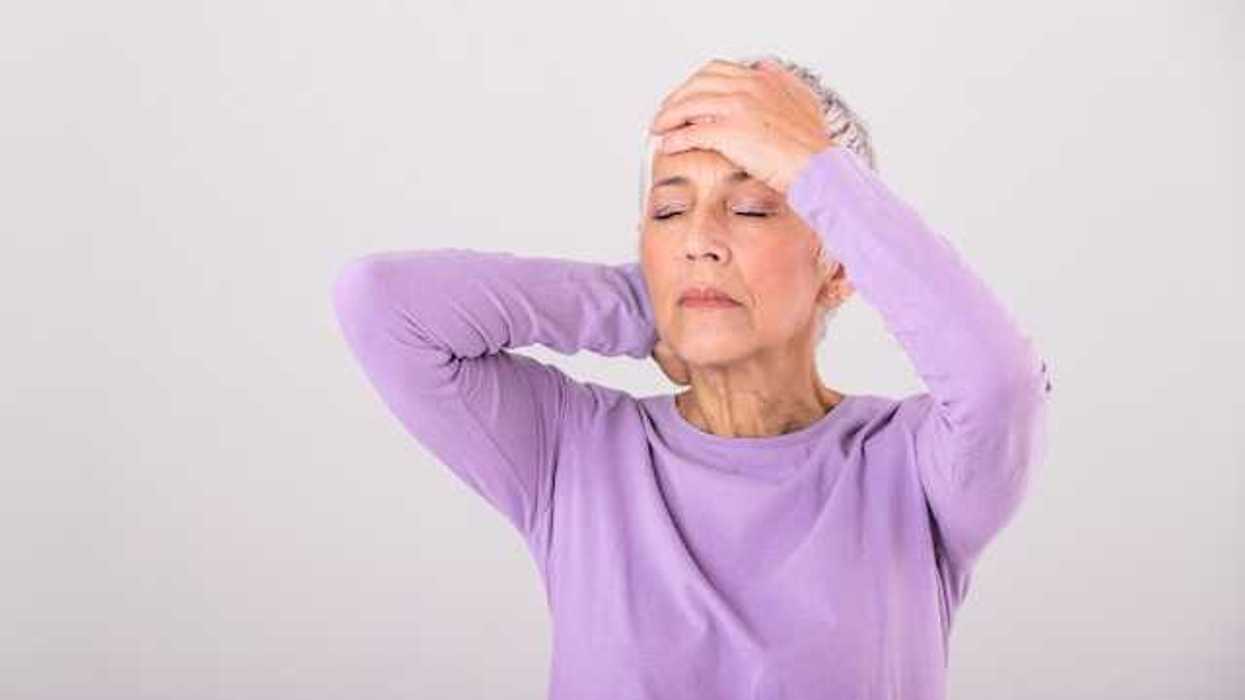An older woman in a lavender shirt holding a hand to her head