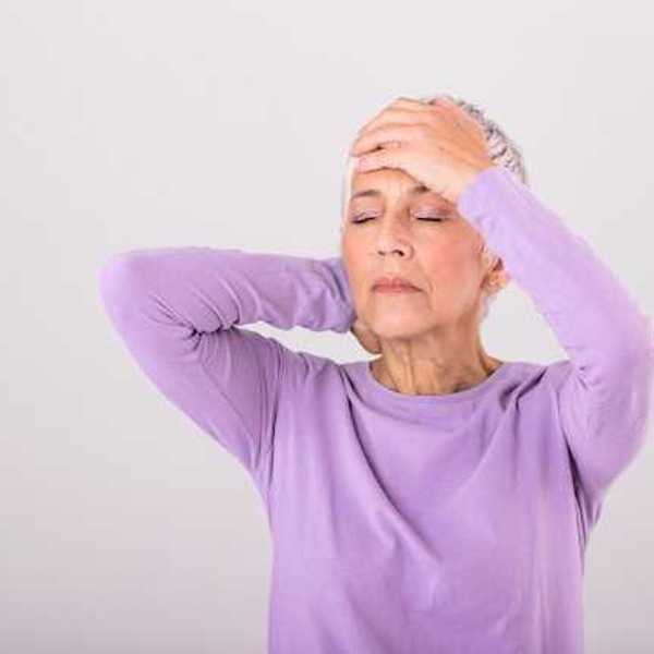 An older woman in a lavender shirt holding a hand to her head