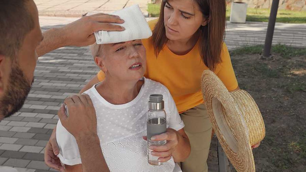 An older woman with a bottle of water being taken care of by two other people during a heat wave