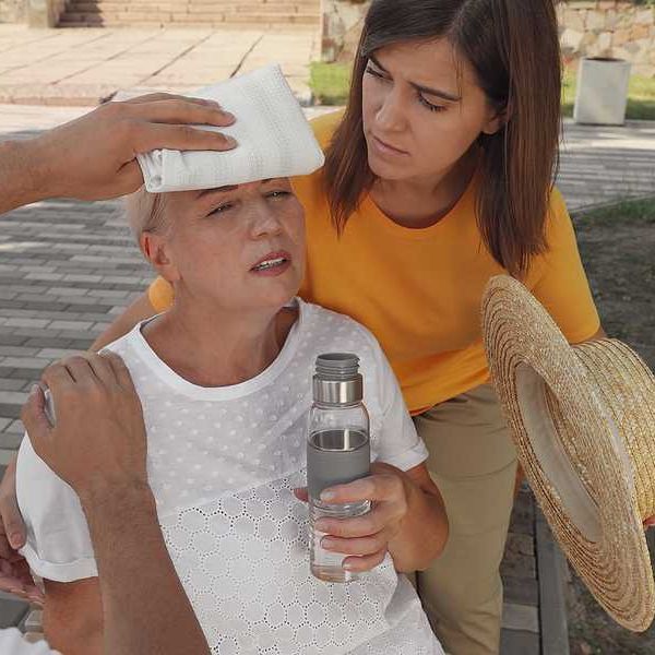 An older woman with a bottle of water being taken care of by two other people during a heat wave