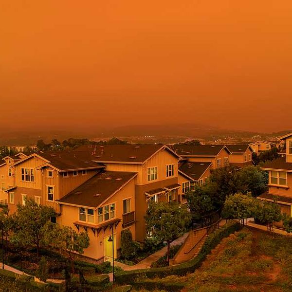 An orange-tinged sky and houses during a wildfire