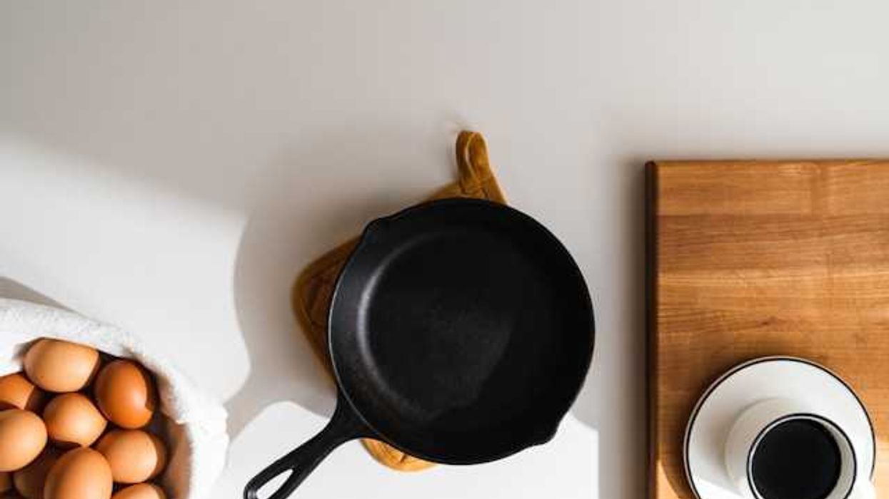 An overhead view of a cast iron pan, a bowl of eggs, and a cup of coffee