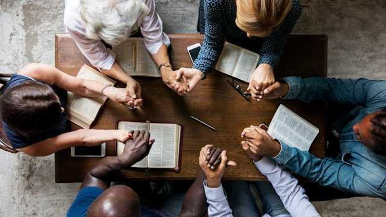 An overhead view of a group of people at a table holding hands and reading the Bible