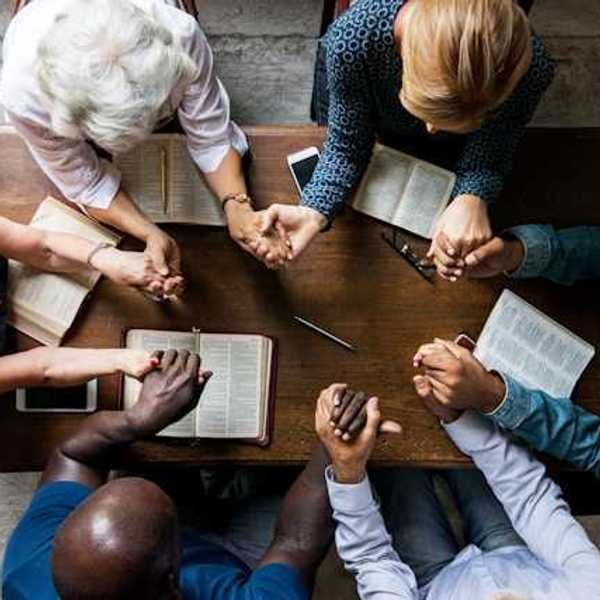 An overhead view of a group of people at a table holding hands and reading the Bible