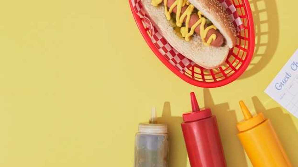 An overhead view of a hot dog with condiments against a yellow background