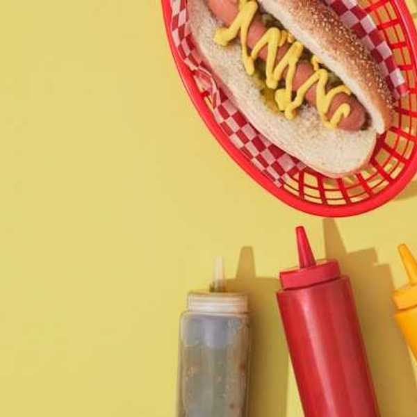 An overhead view of a hot dog with condiments against a yellow background