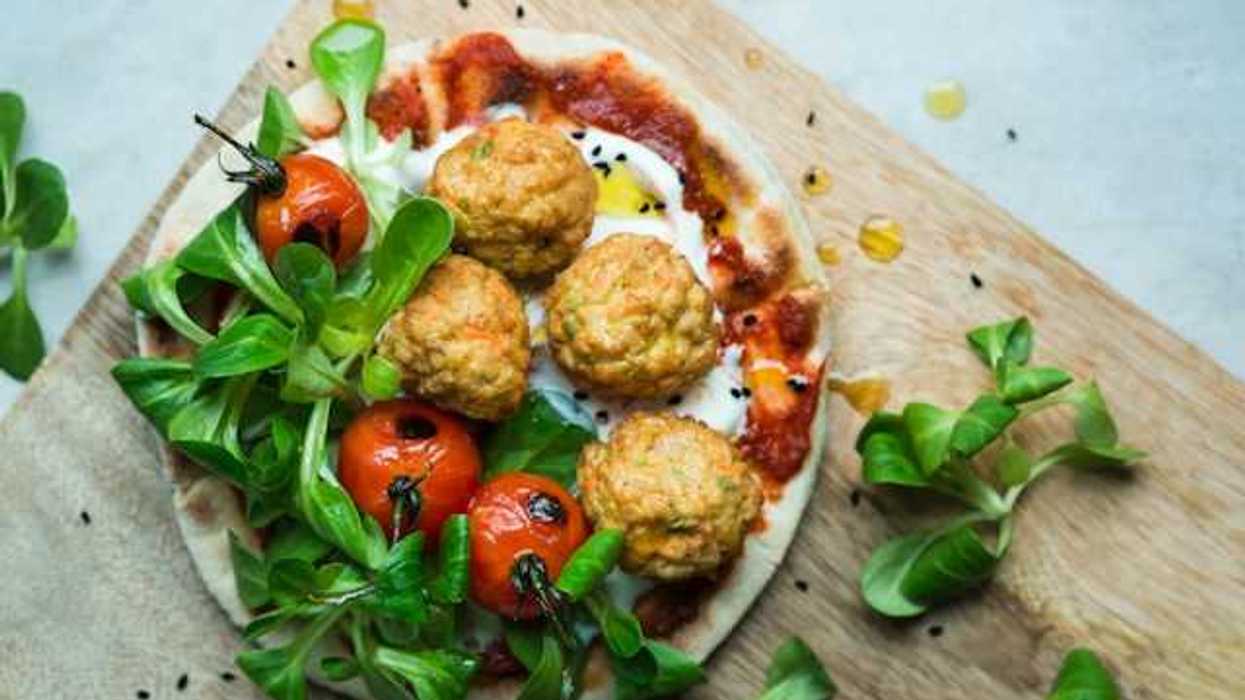 An overhead view of a plate of plant based meatballs and tomatoes on pizza dough