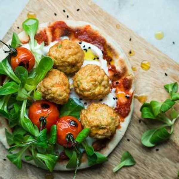 An overhead view of a plate of plant based meatballs and tomatoes on pizza dough