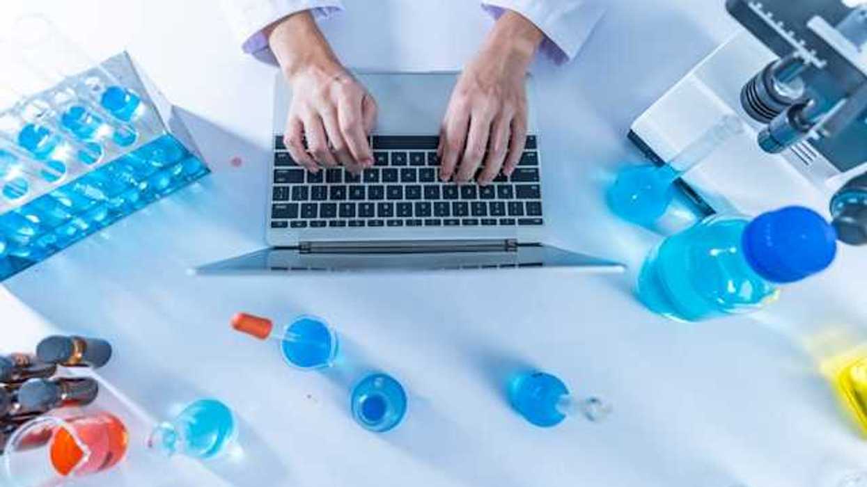An overhead view of a table in a science lab with a the hands of someone typing on a laptop