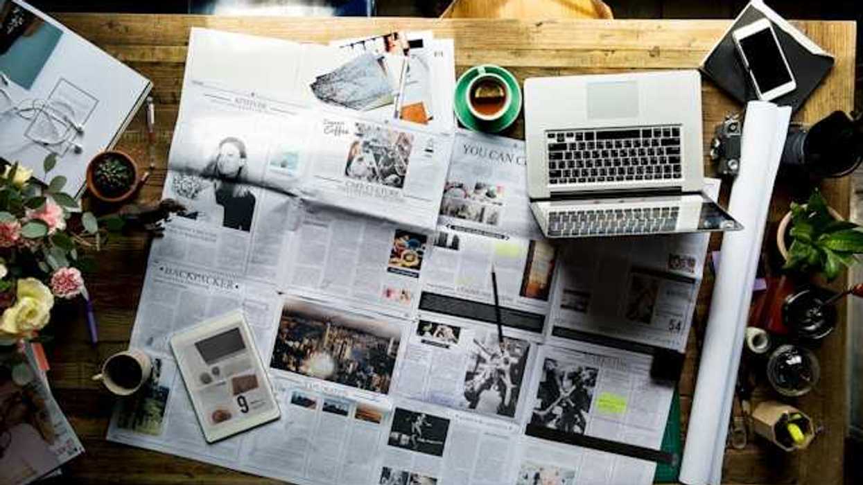 An overhead view of a table with a newspaper, a tablet, and a laptop on it