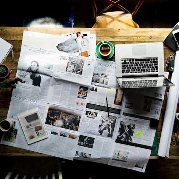 An overhead view of a table with a newspaper, a tablet, and a laptop on it