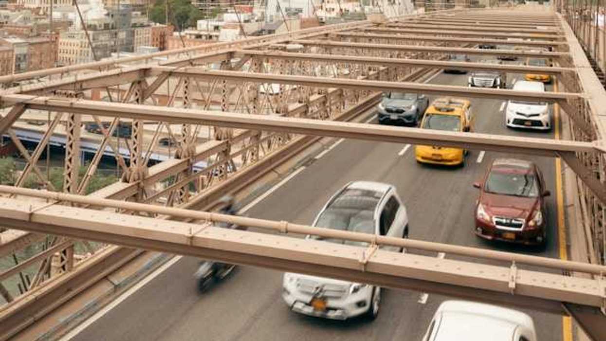 An overhead view of cars driving across a bridge with a city skyline in the background