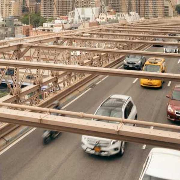 An overhead view of cars driving across a bridge with a city skyline in the background