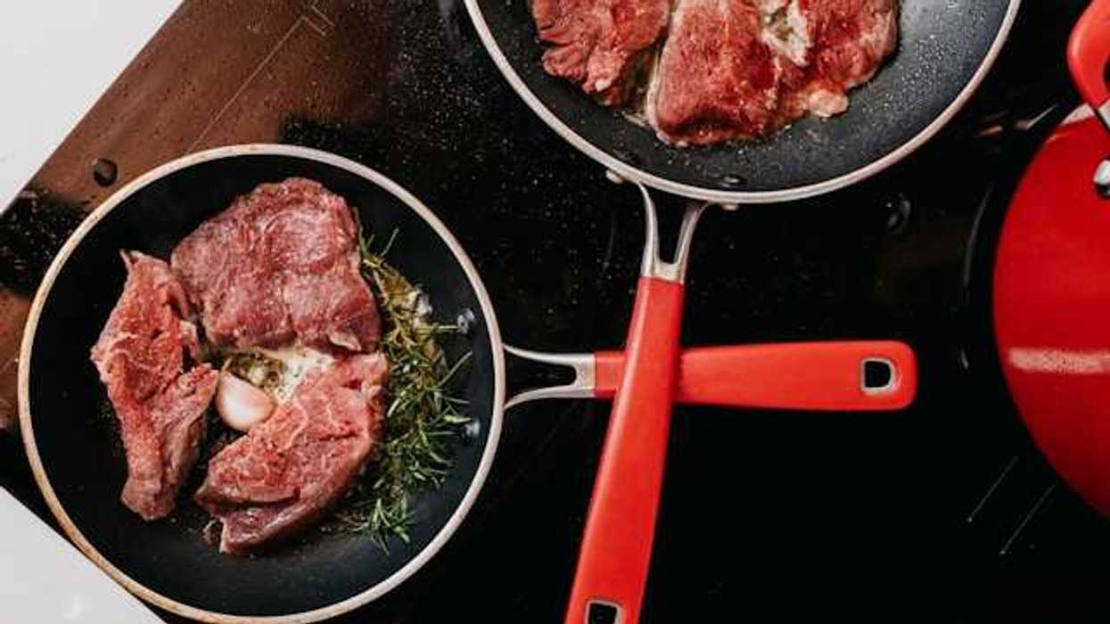 An overhead view of two pans with cooking meat on a stove