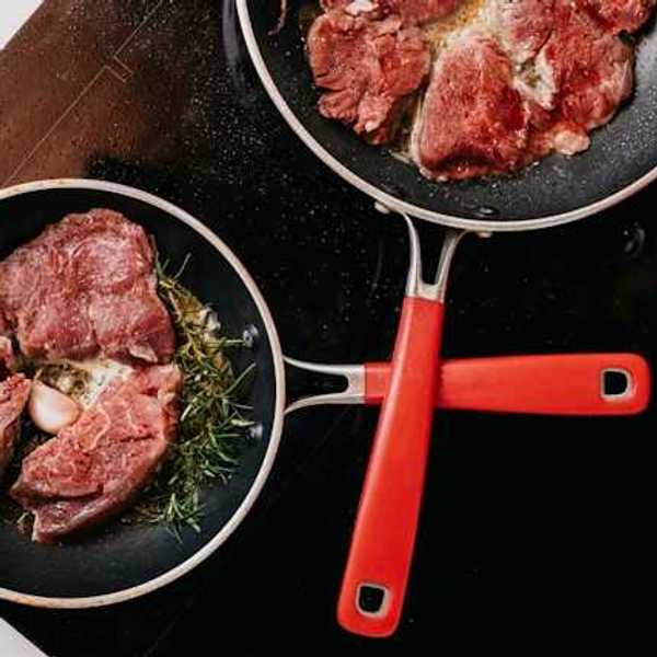 An overhead view of two pans with cooking meat on a stove