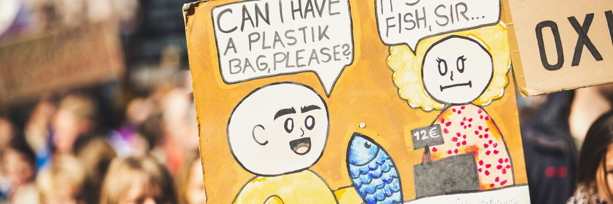 An protester holding a sign with a cashier telling a customer that their plastic bag is in the fish they're buying