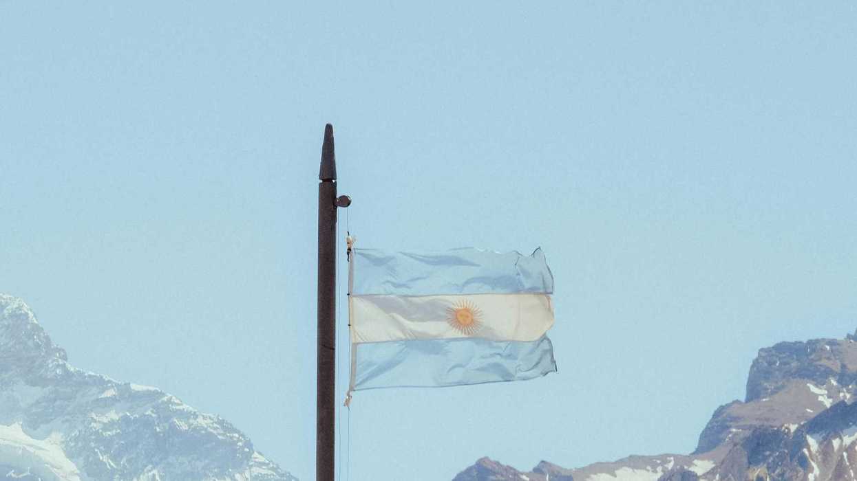 Argentinian flag waves in front of snowy mountains.
