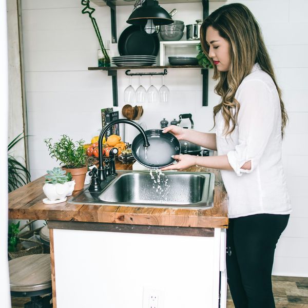 Asian woman wearing white blouse washing ceramic cooking dish under the faucet.