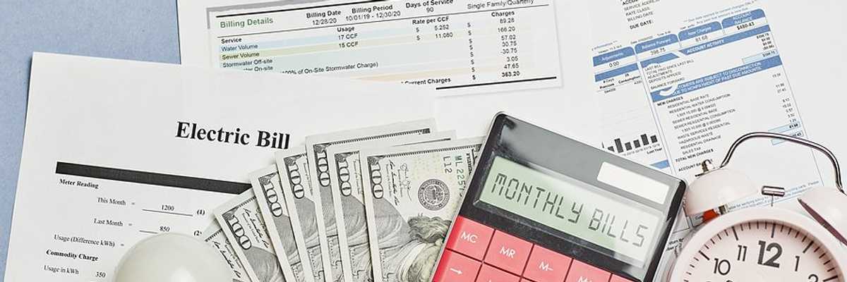 Assorted utility bills with cash, a calculator, and a timer on top of them.