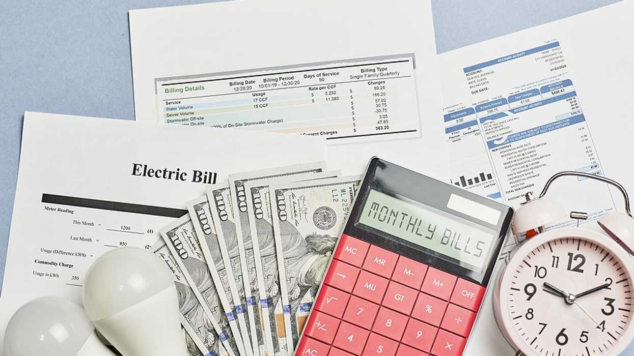 Assorted utility bills with cash, a calculator, and a timer on top of them.