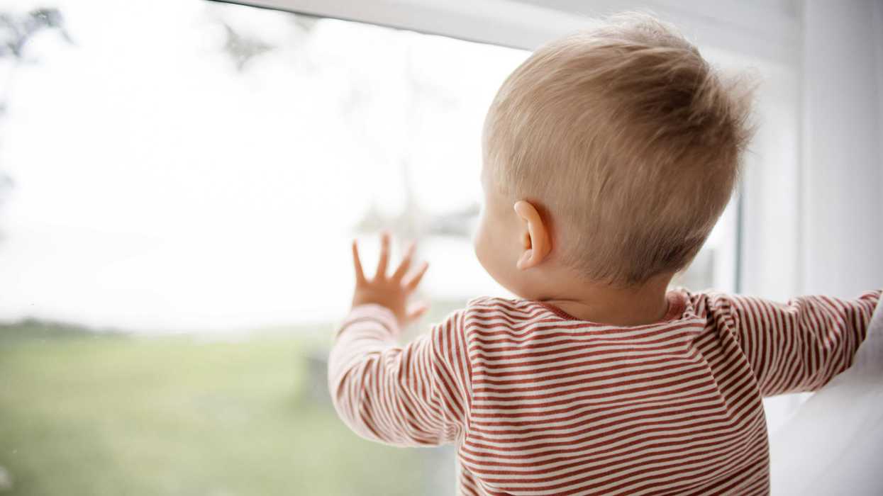 Baby in red and white striped shirt looking out the window.