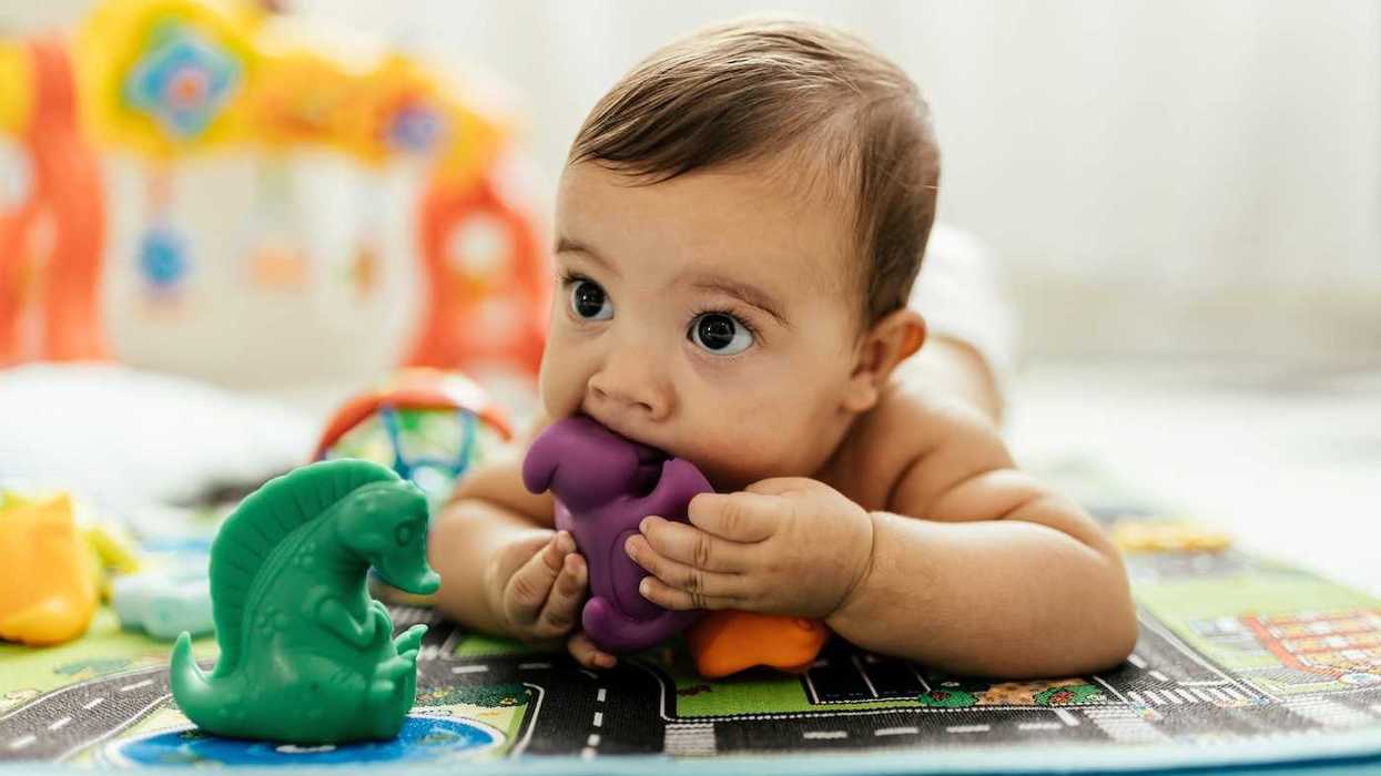 Baby lying on the floor teething on a purple, plastic toy