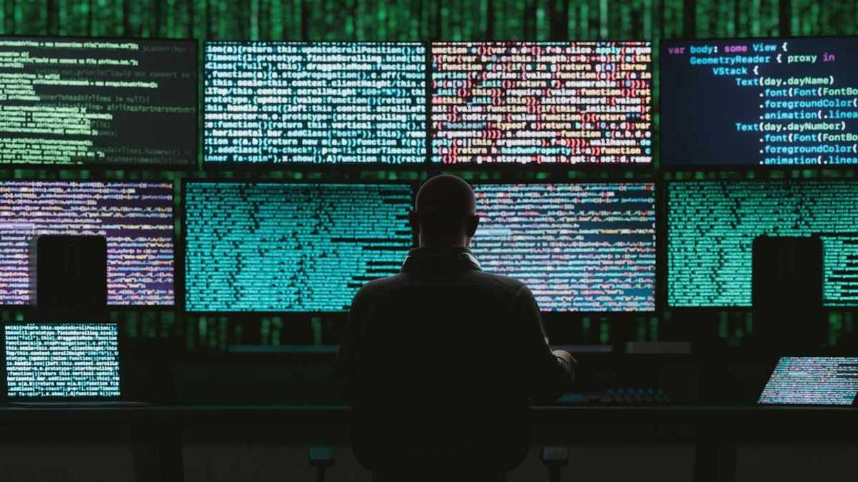 Back of a seated person monitoring data and digital code on multiple monitors