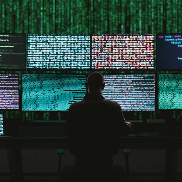 Back of a seated person monitoring data and digital code on multiple monitors