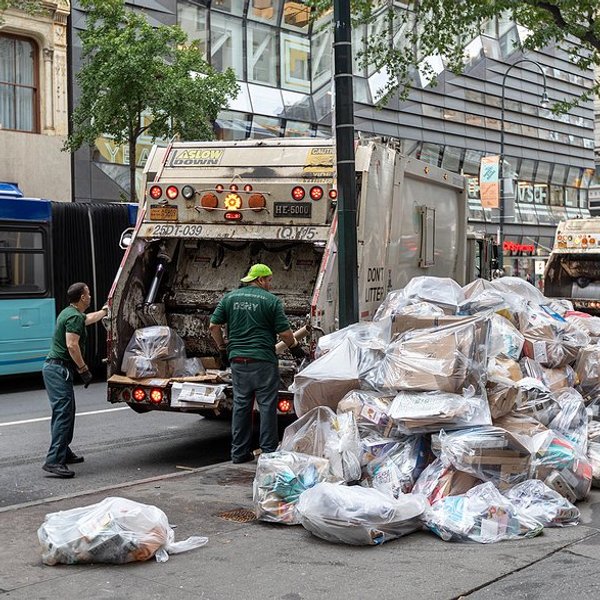Bags of trash on a New York street being loaded into a dump truck