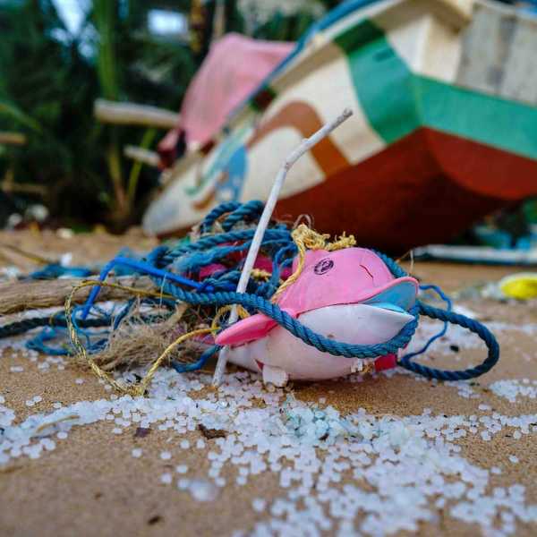 Beach plastic consisting of plastic nurdles, rope and twine, pink and white dolphin toy with a beached boat in the background