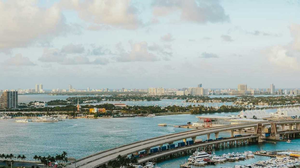 Biscayne Bay, Florida. MacArthur Causeway arches over the tranquil water, connecting to a vibrant marina brimming with yachts. In the distance, the iconic Miami Beach skyline.