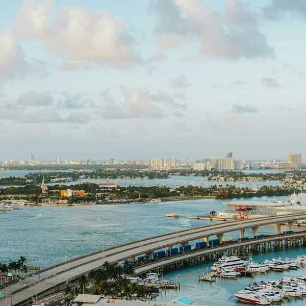 Biscayne Bay, Florida. MacArthur Causeway arches over the tranquil water, connecting to a vibrant marina brimming with yachts. In the distance, the iconic Miami Beach skyline.