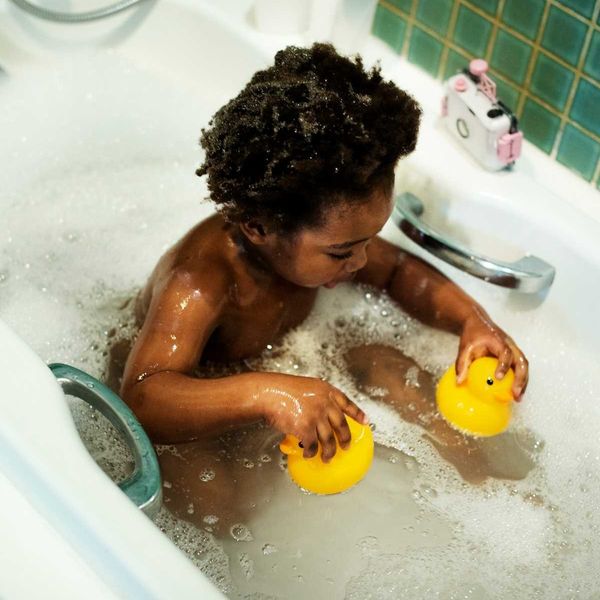 Black child in bath tub playing with phthalate-laden rubber ducks