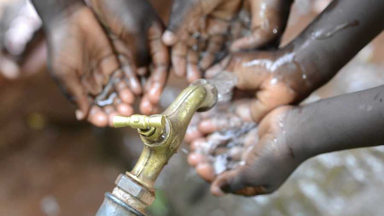 Black children holding their hands under a faucet with water coming out of it