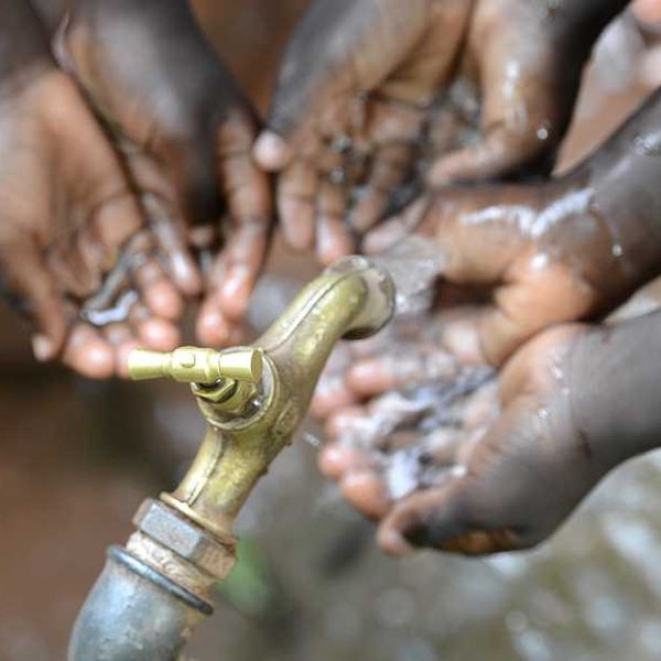 Black children holding their hands under a faucet with water coming out of it