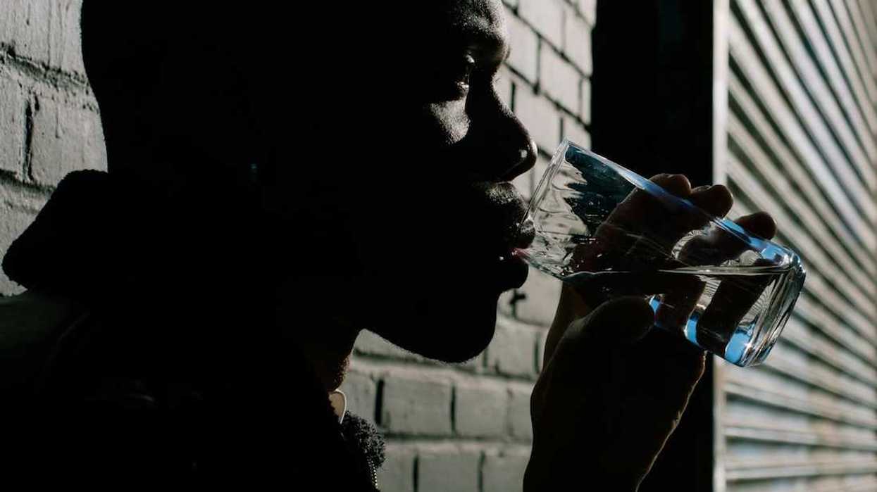 Black man leaning against brick wall drinking from a water glass