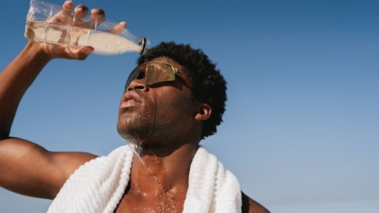 Black man pouring water over his head on a hot day with blue ocean in background.